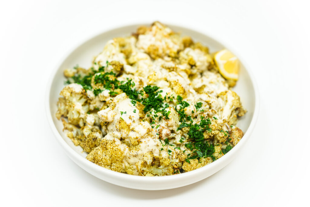 Za'atar stir-fried cauliflower topped with a creamy tahini aioli, garnished with fresh parsley, showcasing tender, spiced cauliflower florets with a rich, tangy sauce.