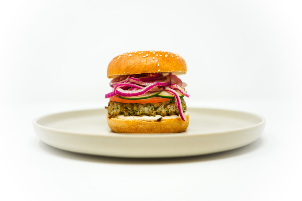 A juicy Mediterranean Herb and Tahini Chicken Burger with fresh herbs, creamy tahini aioli, and crisp veggies on a toasted sesame bun