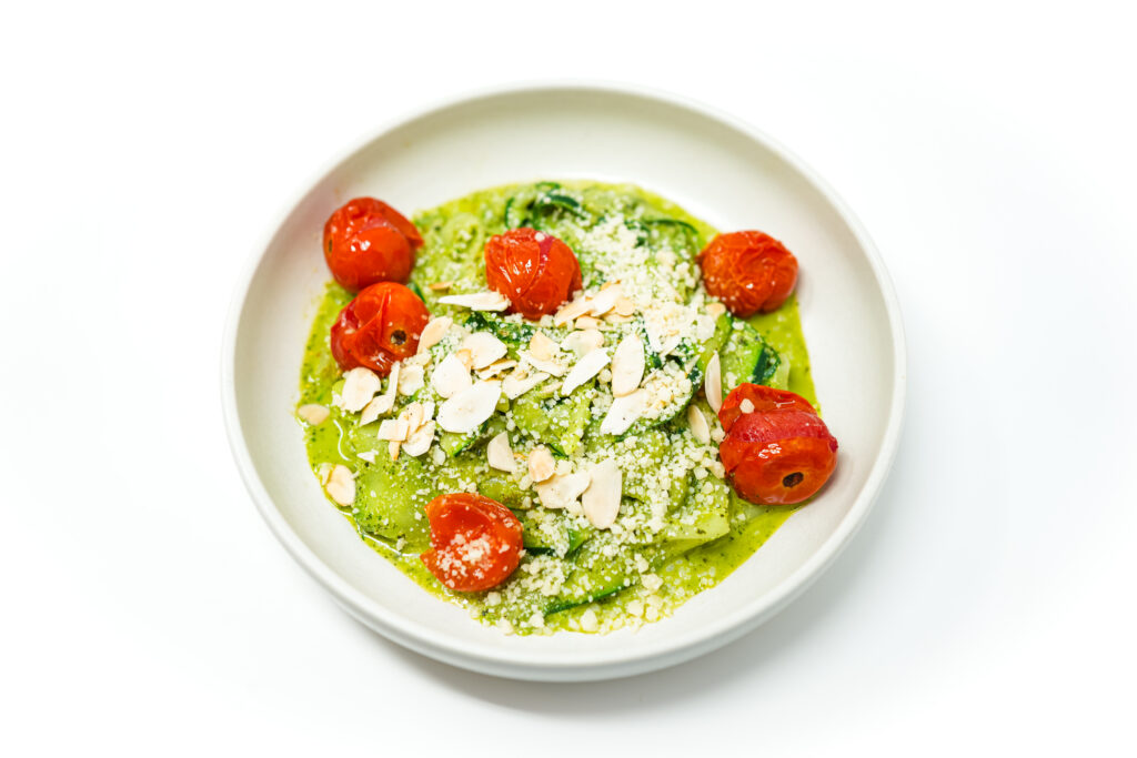 A vibrant plate of zucchini noodles tossed in creamy pesto, topped with roasted cherry tomatoes and garnished with toasted almond slices and Parmesan cheese