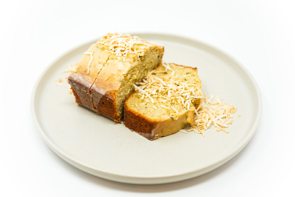 A slice of Coconut Lime Zucchini Bread on a plate, topped with a glossy lime glaze, showcasing its moist interior with flecks of zucchini and coconut, ready to be enjoyed