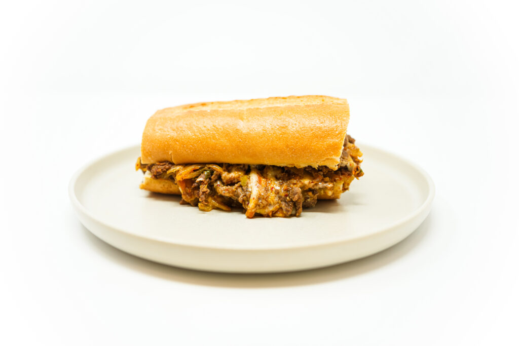 A Beef Bulgogi Cheesesteak on a toasted hoagie roll, filled with marinated Korean beef, sautéed vegetables, kimchi, and melted cheese, creating a savory and flavorful fusion sandwich.
