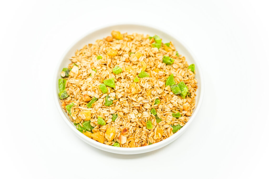 A bowl of Tropical Kiwi Pineapple Granola featuring golden oats, vibrant dried kiwi and pineapple pieces, crunchy macadamia nuts, and coconut flakes, showcasing a colorful and textured mix perfect for breakfast or snacking.