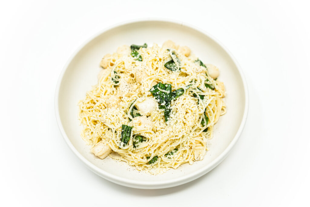 A plate of Lemon Basil Scallop Angel Hair featuring golden seared scallops atop delicate angel hair pasta, coated in a vibrant lemon garlic sauce, and garnished with fresh basil leaves and grated Parmesan cheese.