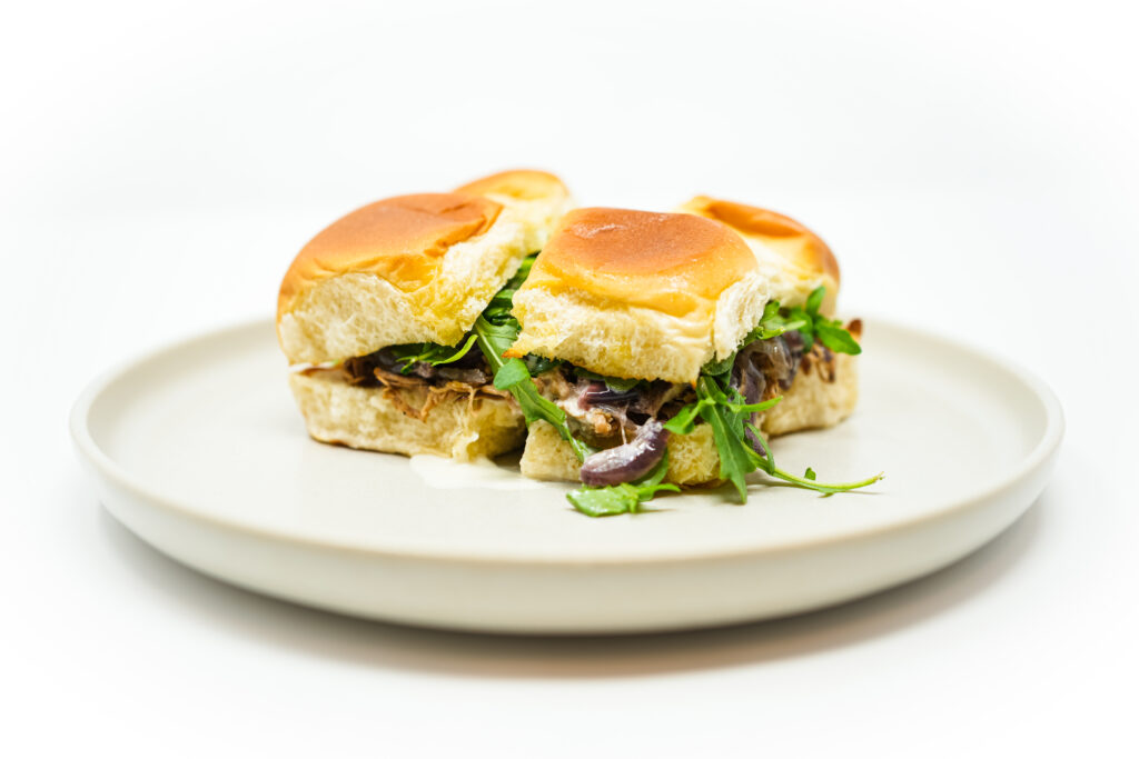 Braised Pork Tenderloin Sliders with Horseradish Aioli, topped with caramelized onions and fresh arugula, served on soft slider buns.
