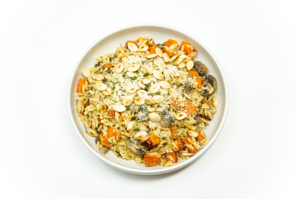 A plate of brown butter orzo with roasted butternut squash, sautéed mushrooms, and toasted squash seeds, garnished with fresh thyme and Parmesan cheese, offering a warm, earthy, and seasonal dish.