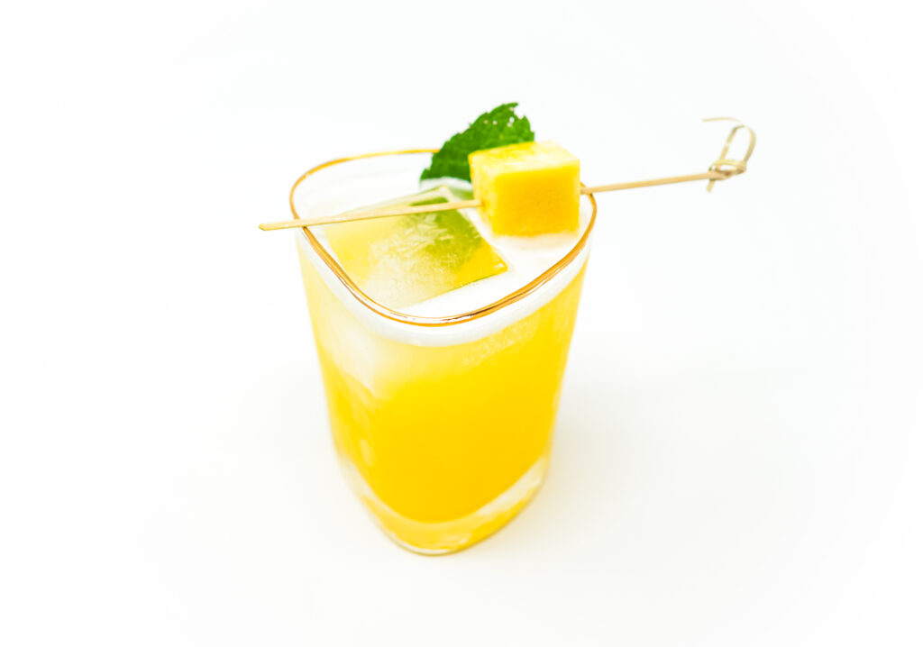 A refreshing Pineapple Sotol Smash cocktail served in a rocks glass with ice, garnished with a slice of fresh pineapple and a sprig of mint, showcasing its vibrant tropical colors and inviting presentation.