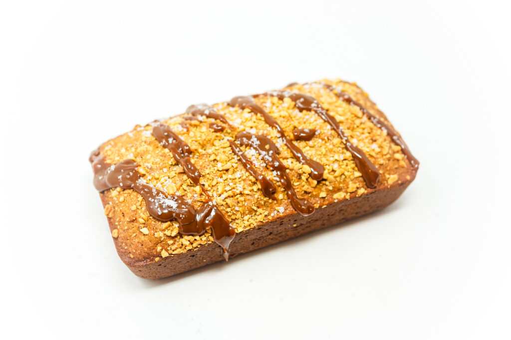 A loaf of Sea Salted Caramel Peanut Banana Bread topped with roasted peanuts and drizzled with a rich caramel sauce.