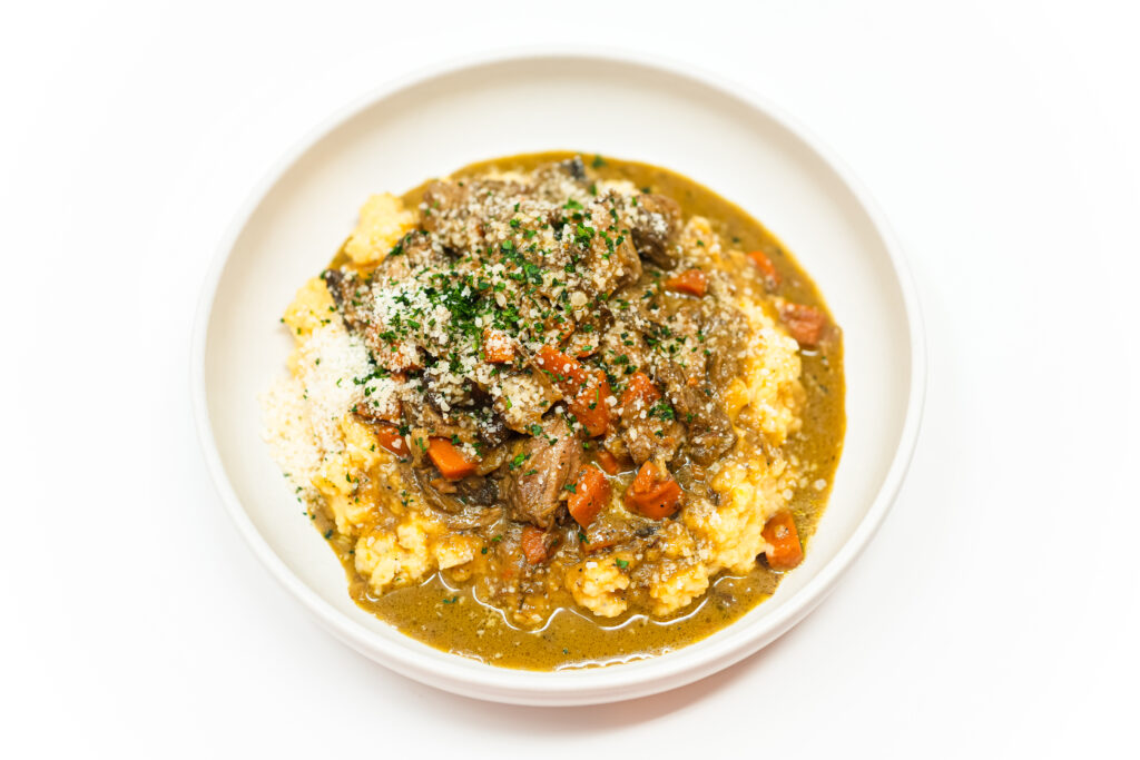 A hearty plate of veal and mushroom stew with carrots, served over creamy mashed rutabaga. The dish is garnished with fresh parsley and a generous sprinkle of Parmesan cheese, creating a comforting and flavorful meal.