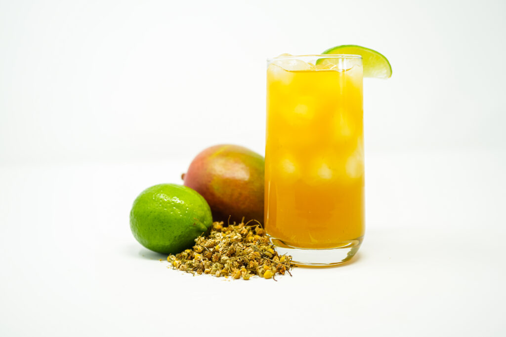 A glass of chamomile mango lime tea, garnished with a lime slice, with a vibrant yellow hue from mango nectar