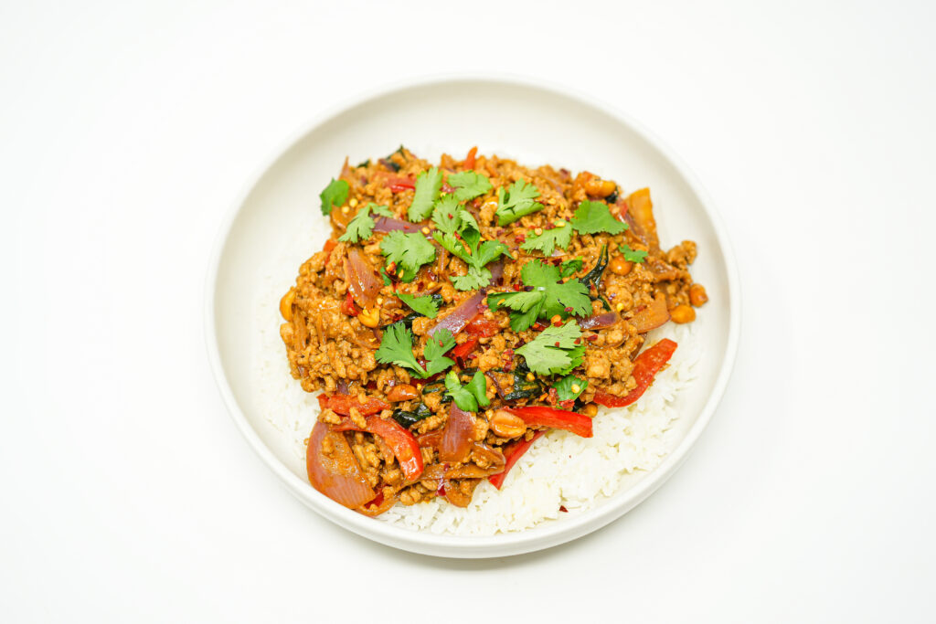 A vibrant Thai-inspired peanut and ground beef stir-fry served over jasmine rice, featuring sliced red bell peppers, julienned carrots, roasted peanuts, and torn basil, with a drizzle of lime juice and fresh cilantro garnish.