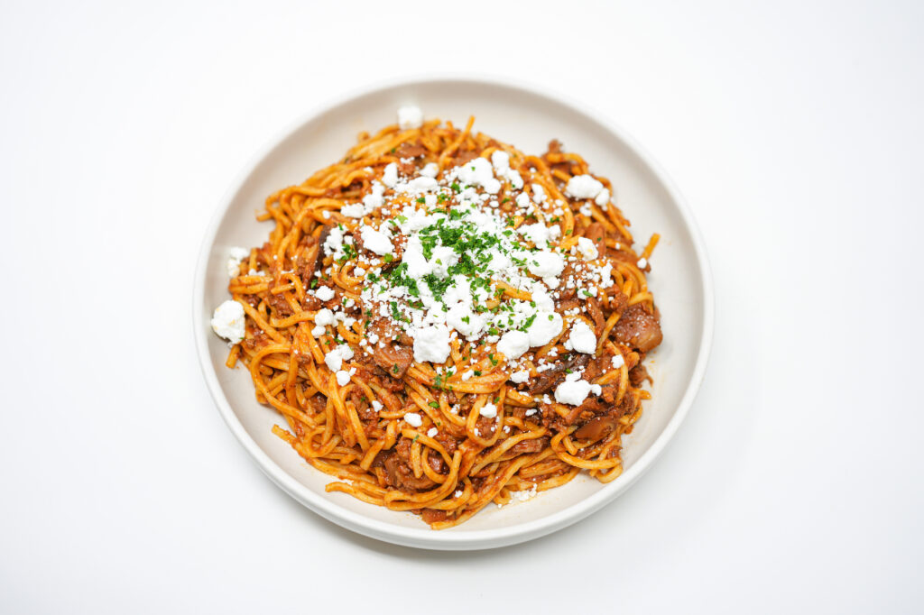 A plate of spaghetti topped with rich Lamb and Mushroom Bolognese, garnished with crumbled goat cheese and fresh parsley.