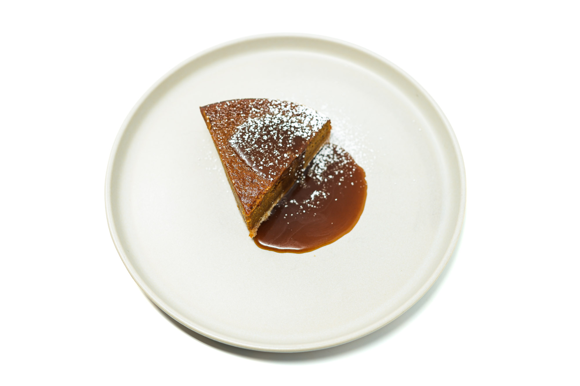 A slice of Sweet Potato Pie with a vanilla wafer crust, drizzled with whiskey caramel sauce and dusted with powdered sugar.