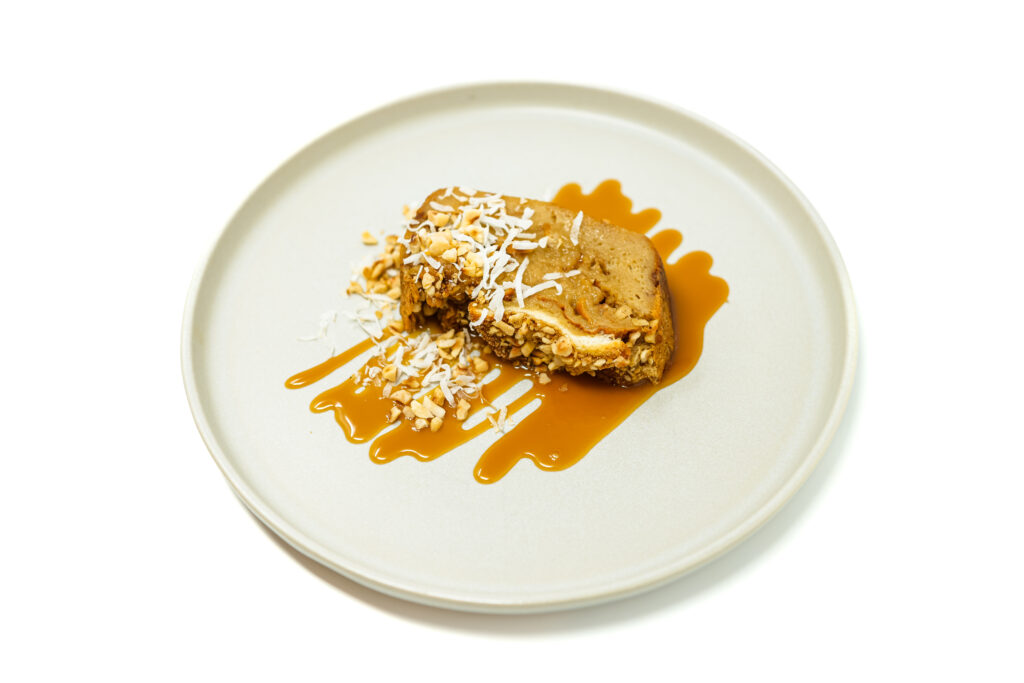 Hawaiian Roll Macadamia Nut Bread Pudding topped with coconut caramel sauce, served in slices with macadamia nuts and a drizzle of caramel.