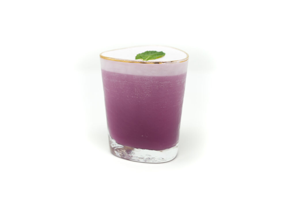 A frothy Pomegranate Pineapple Smoke cocktail in a rocks glass, featuring a silky egg white foam top and vibrant pink hues, set against a clean, minimal background.