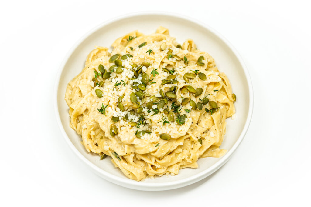 A bowl of White Pumpkin Fettuccine Alfredo topped with fresh thyme, toasted pumpkin seeds, and grated Parmesan, showcasing creamy pasta with a rich pumpkin sauce.
