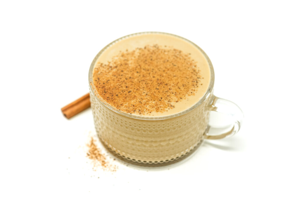 Glass of creamy espresso martini eggnog topped with a dusting of nutmeg, accompanied by a cinnamon stick, on a white background.