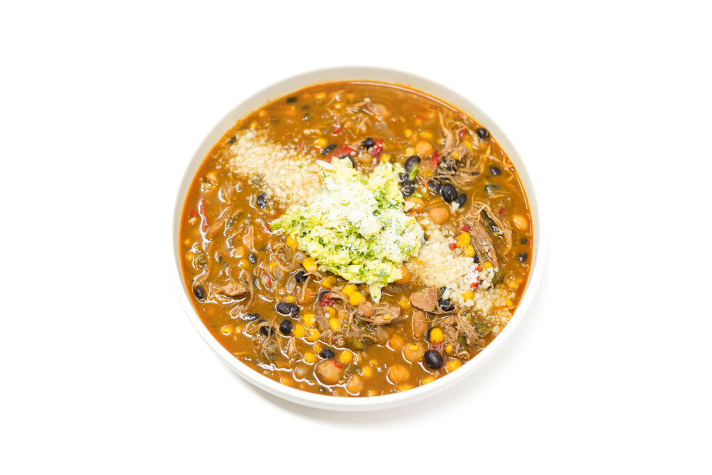 A hearty bowl of Chipotle Chicken and Chickpea Stew featuring tender shredded chicken, creamy chickpeas, corn, and a smoky chipotle-infused broth, topped with lime-dressed cabbage, crumbled cotija cheese, and fresh cilantro.