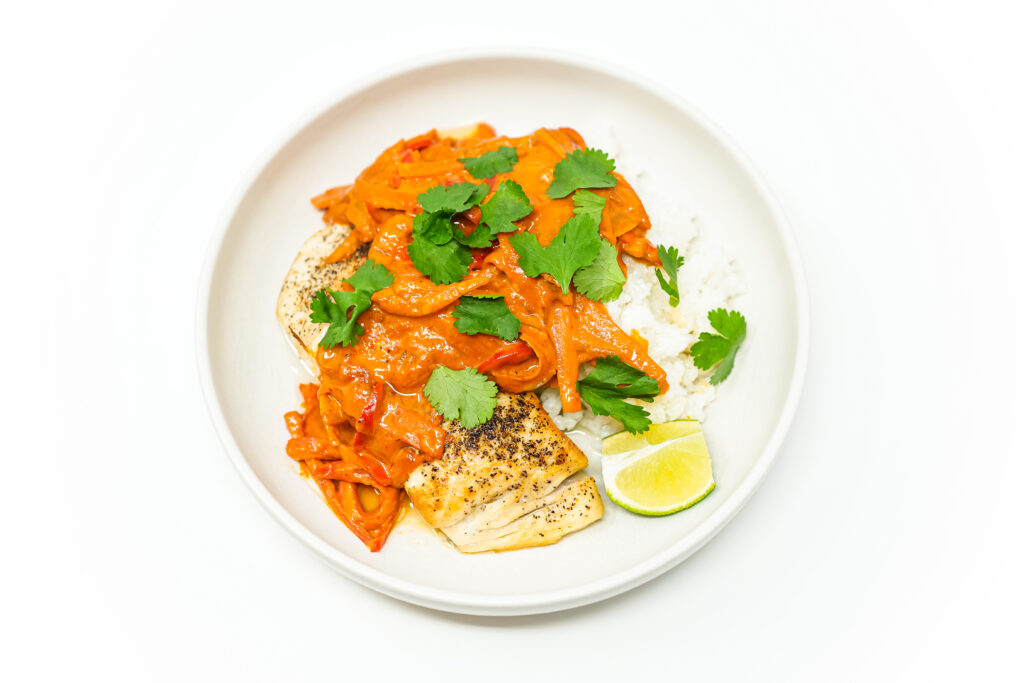 A pan seared amberjack fillet topped with creamy coconut curry sauce, garnished with fresh cilantro and served alongside steamed rice and lime wedges.