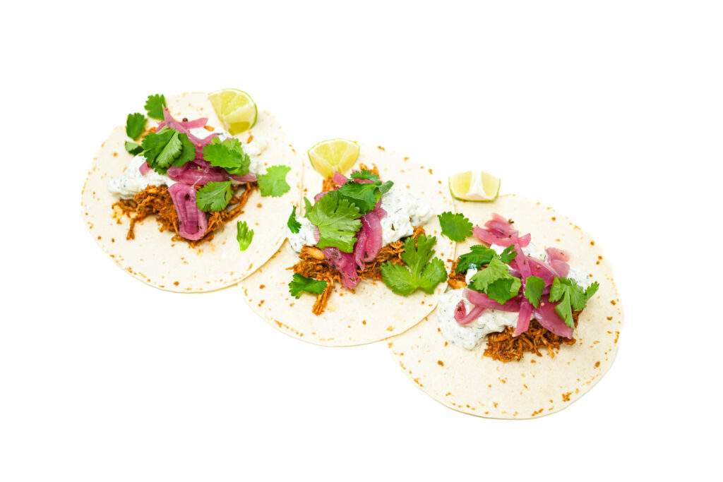 A close-up image of Chicken Tikka Masala Tacos filled with spiced shredded chicken, creamy yogurt slaw, and vibrant pickled red onions, garnished with fresh cilantro and lime wedges, served on warm tortillas.