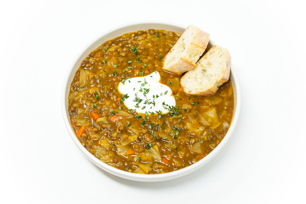 A steaming bowl of Pumpkin, Cabbage, and Lentil Stew with a velvety, golden broth, tender cabbage, and hearty lentils, garnished with fresh thyme and a dollop of sour cream, served alongside crusty bread.