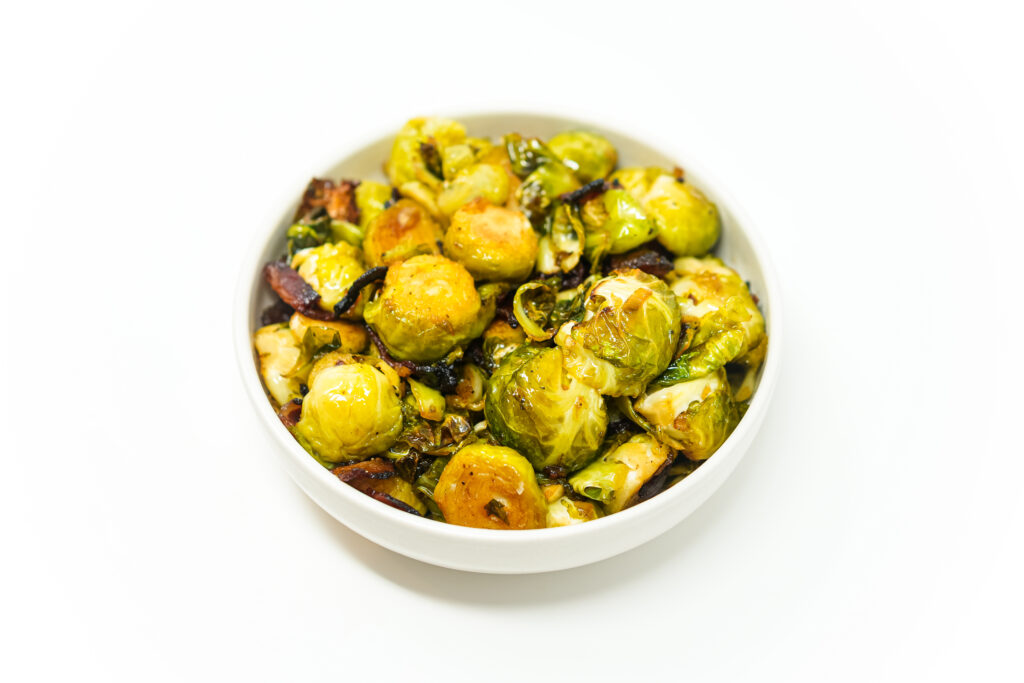 A plate of Maple Bacon Glazed Brussels Sprouts, featuring golden caramelized sprouts coated in a maple-balsamic glaze, with crispy bacon pieces and a sprinkle of paprika.