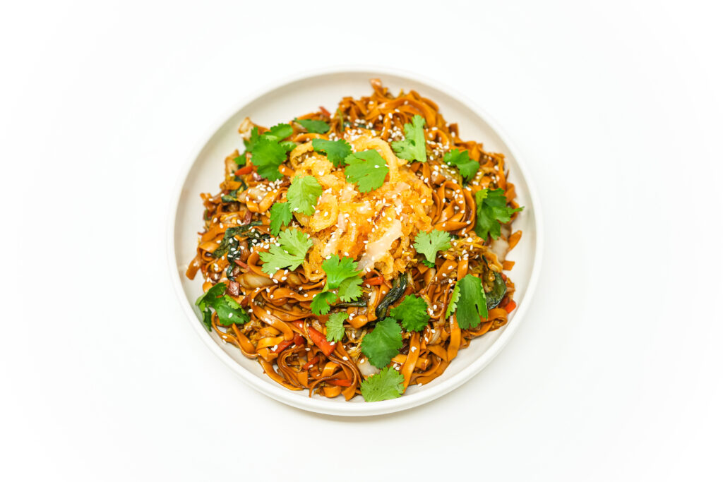 A vibrant bowl of garlic, cabbage, and egg noodle stir fry topped with golden, crispy onion strings, fresh cilantro, and sesame seeds.