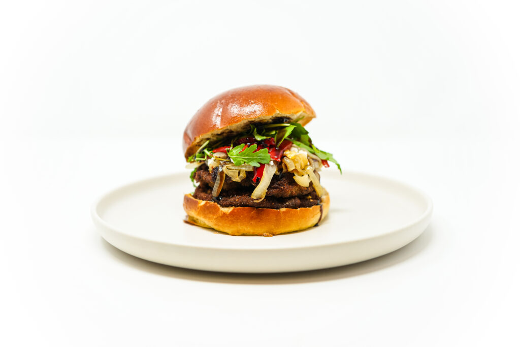 A Mediterranean Crispy Portobello Burger featuring a golden fried portobello mushroom layered with tangy goat cheese, caramelized onions, roasted red peppers, fresh arugula, and a drizzle of balsamic glaze, served on a toasted brioche bun.
