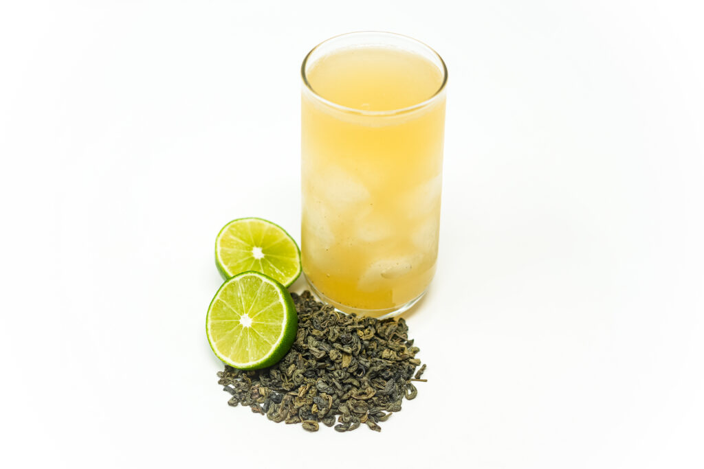 A refreshing glass of Green Tea Limeade served over ice, garnished with fresh lime, showcasing its vibrant citrus and earthy tones.