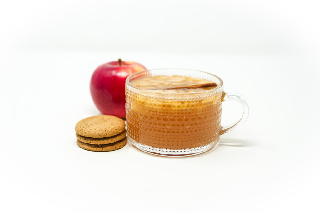 A mug of Orange Wine Glogg with slices of apple, almonds, and a cinnamon stick, surrounded by ginger snap cookies.