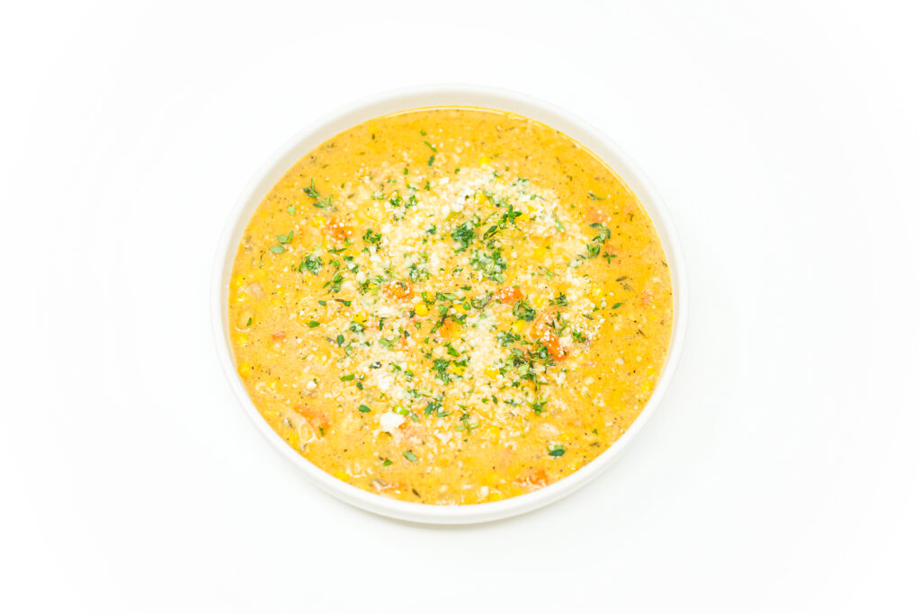 A bowl of creamy corn clam chowder garnished with fresh thyme and grated Parmesan, showcasing the rich, velvety texture and vibrant pops of sweet corn and tender clams.