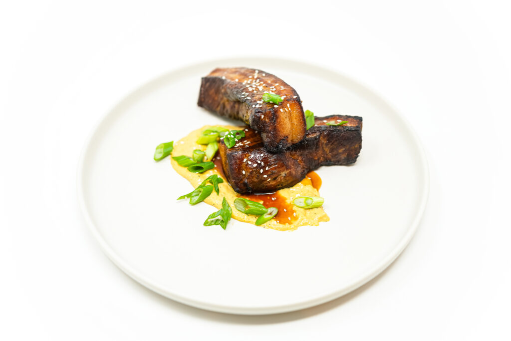Sticky BBQ Pork Belly slices served on a plate, showcasing caramelized, smoky-sweet glaze with crispy edges and tender, juicy layers of meat.