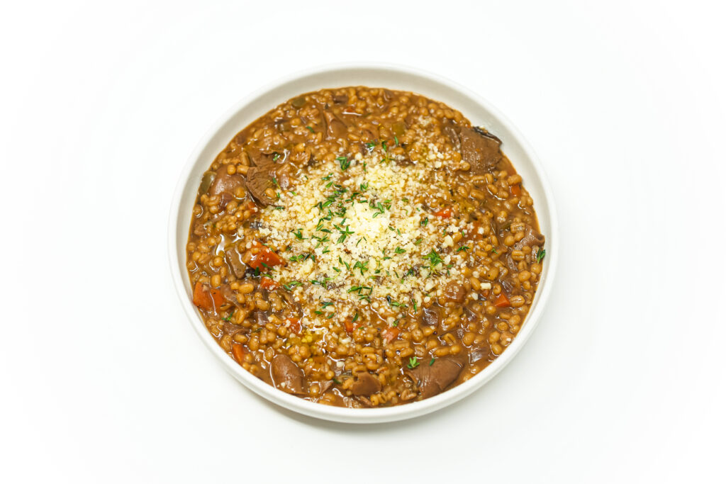Beef Barley and Oyster Mushroom Stew in a white bowl, garnished with fresh herbs and Parmesan cheese, showcasing its hearty texture and rich, flavorful broth.