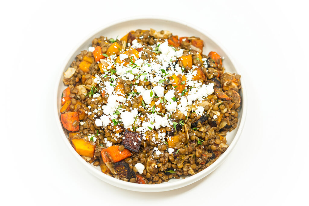 Harvest Lentil Salad with Goat Cheese and Figs in a white bowl, featuring roasted butternut squash, carrots, toasted almonds, and balsamic vinaigrette, garnished with fresh thyme.