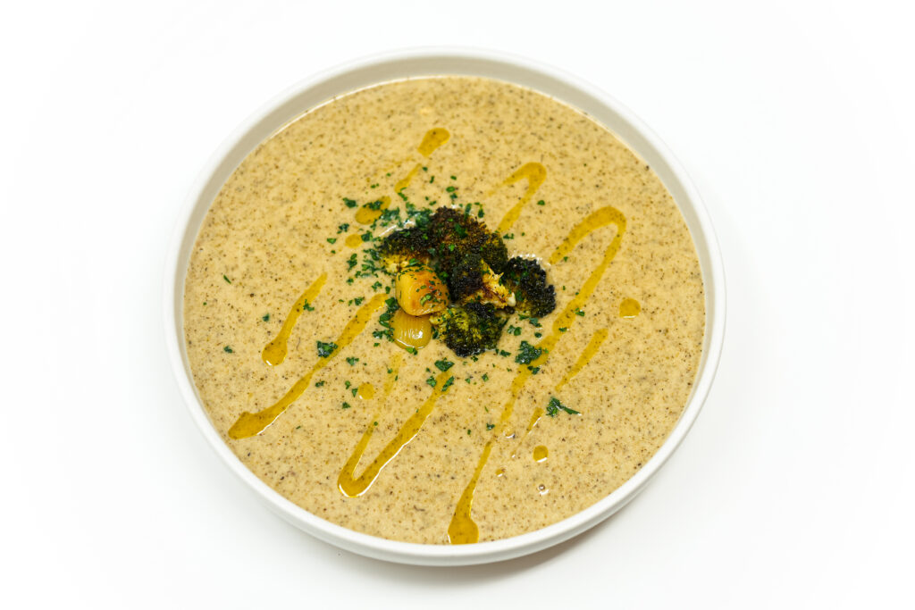 A bowl of Roasted Broccoli and Garlic White Cheddar Soup, garnished with roasted broccoli florets and a drizzle of olive oil, served warm and creamy.
