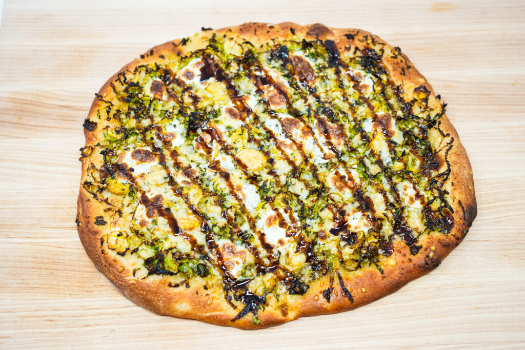 Brussels Sprouts and Parmesan Pizza with a crispy crust, topped with shredded Brussels sprouts, nutty Parmesan cheese, and drizzled with tangy balsamic glaze, served on a rustic wooden board.