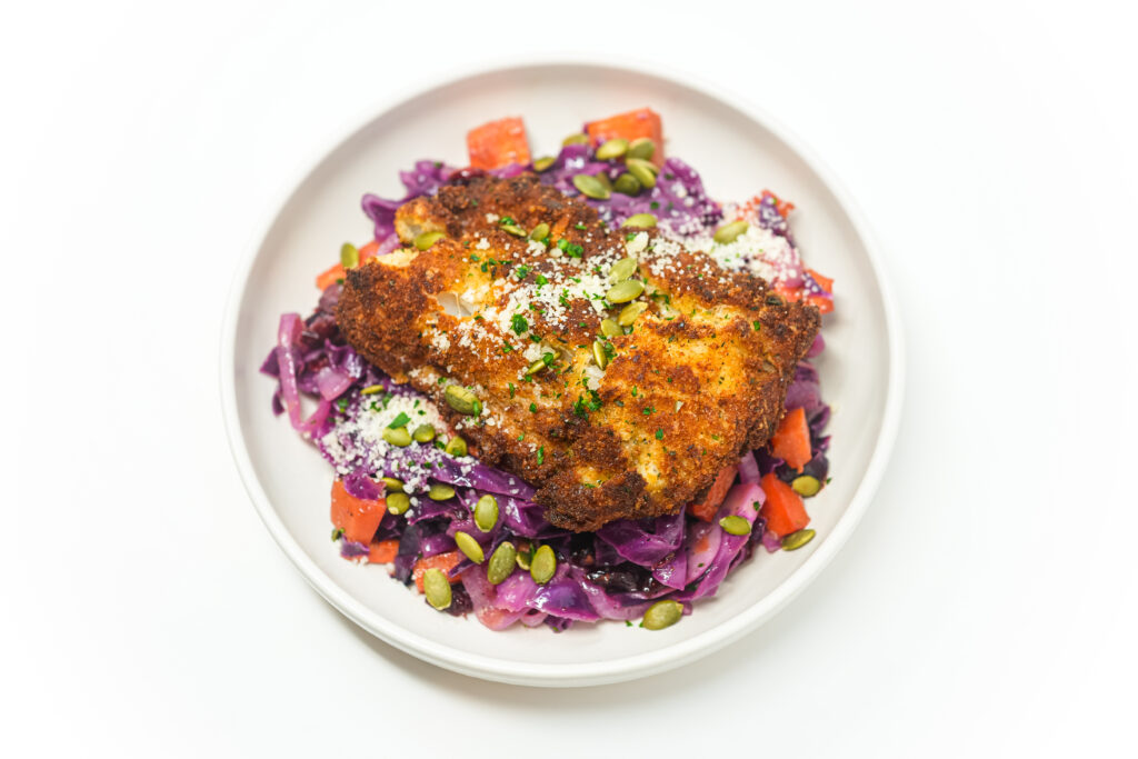 Golden, crispy pan-fried hake fillet with a fragrant herb crust, served alongside a vibrant warm purple cabbage salad, garnished with toasted nuts and fresh herbs.