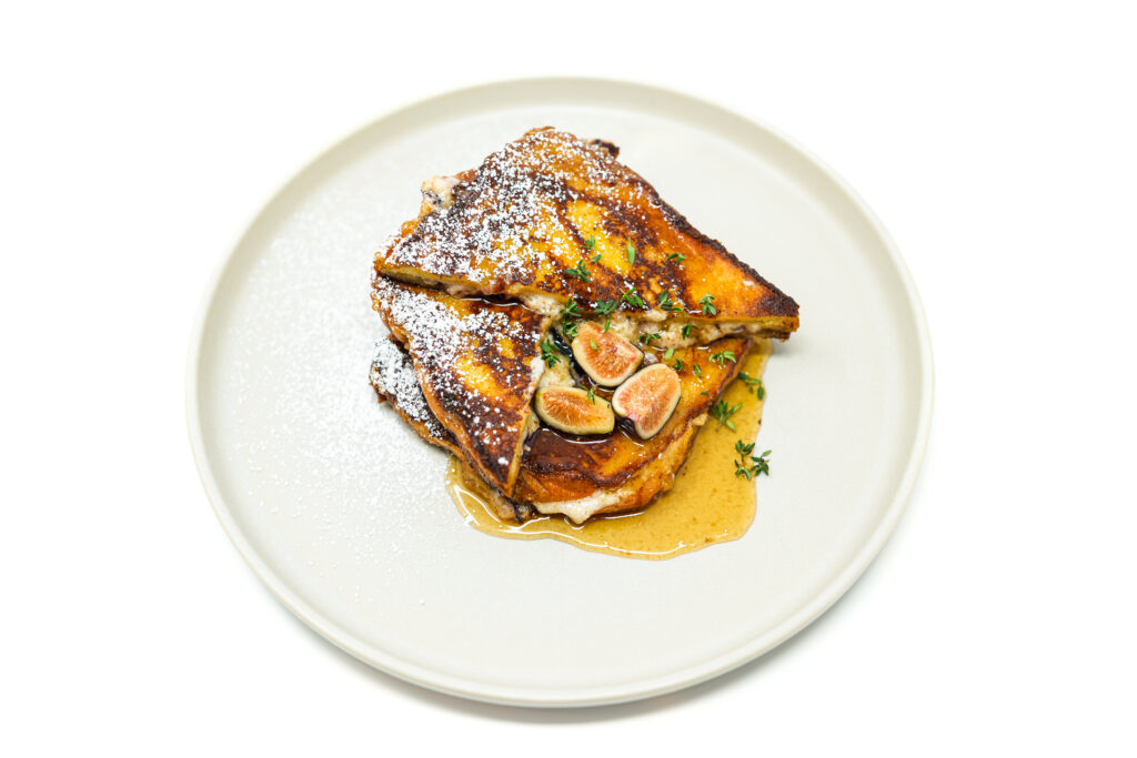 Golden brioche French toast stuffed with creamy mascarpone and fresh figs, drizzled with thyme-infused maple syrup and garnished with sliced figs.