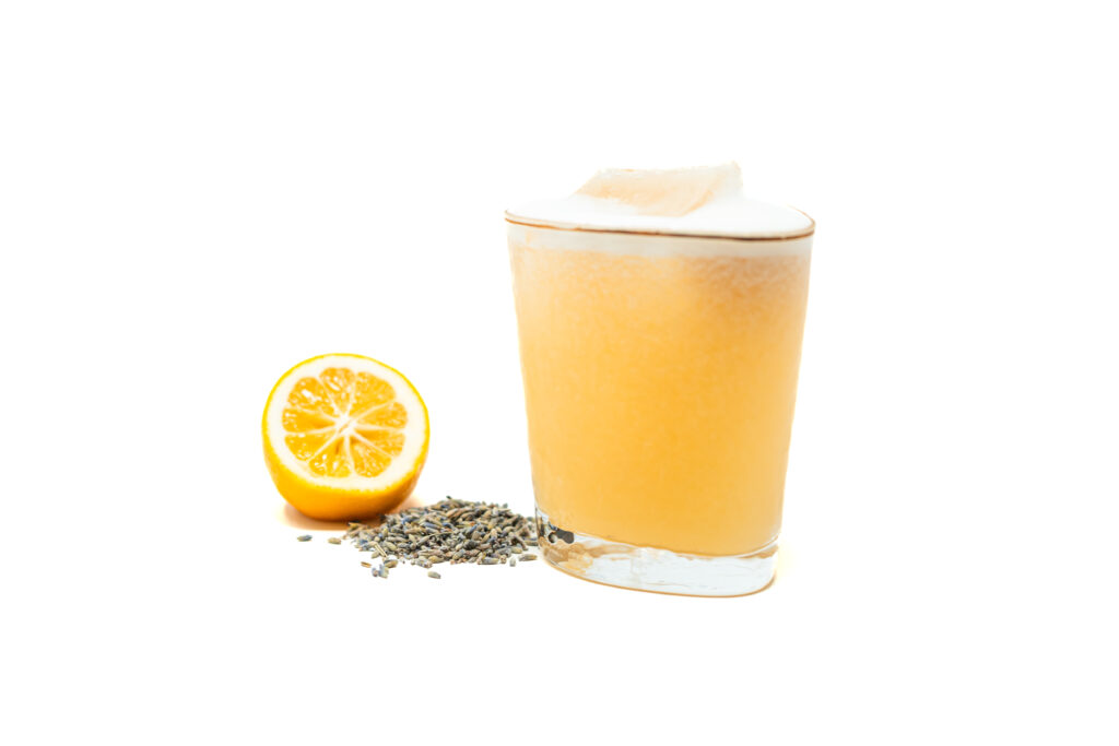 A chilled Lavender Vodka Sour cocktail in a glass, garnished with a fresh Meyer lemon half and dried lavender buds on a white background.