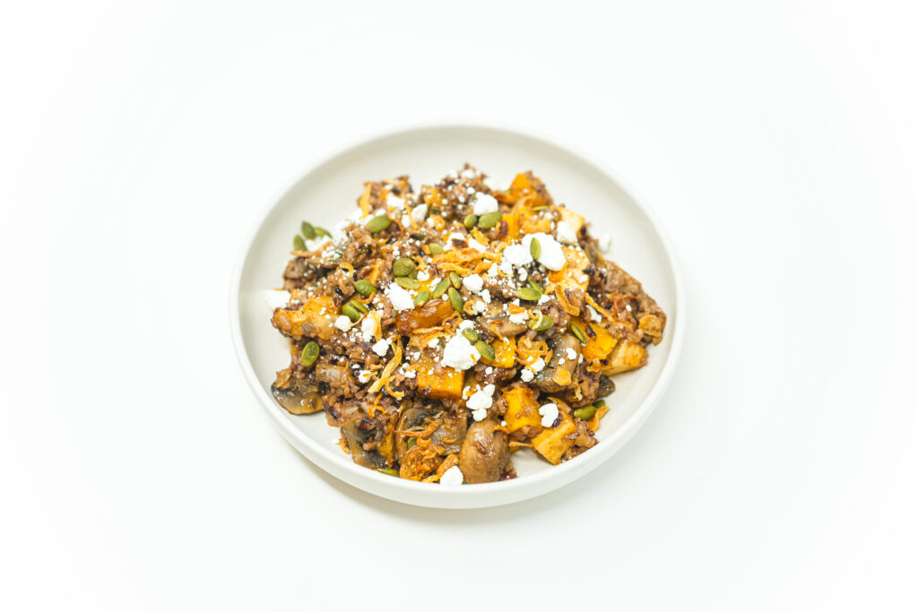 A bowl of wild rice tossed with roasted butternut squash, rutabaga, and mushrooms, topped with crumbled goat cheese, toasted pepitas, and crispy shallots.