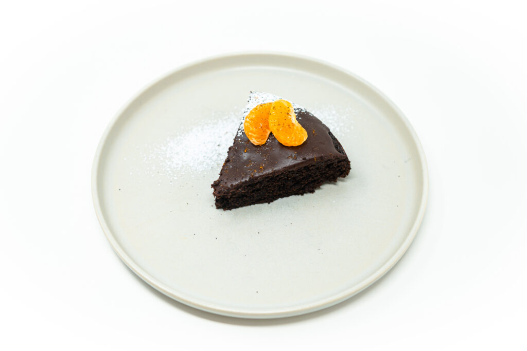 Chocolate Chili Olive Oil Cake with a glossy dark chocolate ganache, garnished with fresh mandarin orange segments and a dusting of powdered sugar, served on a white plate.