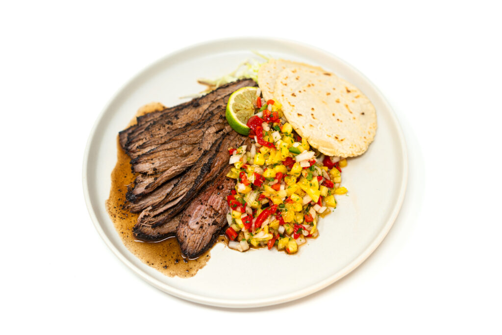 Sliced coffee-rubbed sirloin served with pan au jus and pineapple-mint salsa on a white plate, garnished with fresh herbs.