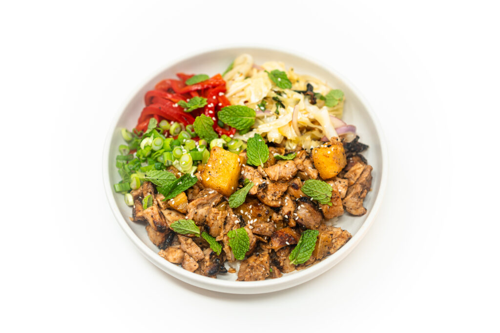 Miso pineapple chicken bowl with charred cabbage salad, roasted red bell peppers, fresh mint, and green onions served in a ceramic bowl