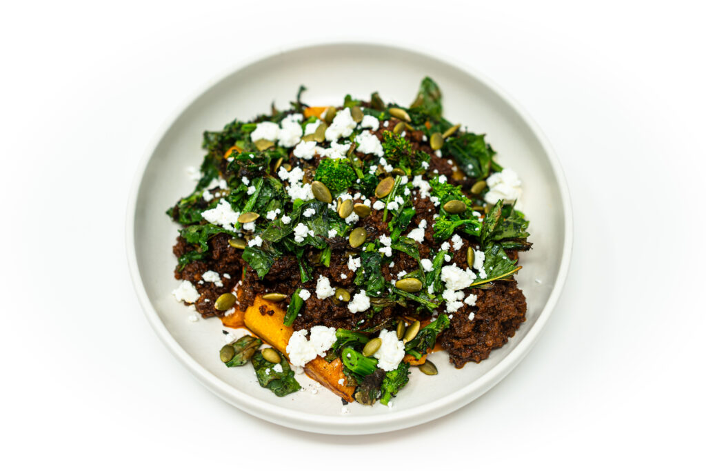 A bowl of miso ground beef with roasted butternut squash, charred rapini, crumbled goat cheese, toasted pepitas, and a drizzle of honey.