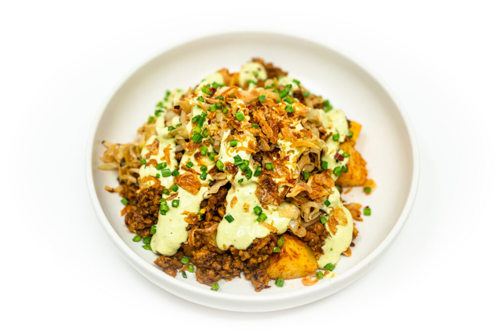 A vibrant bowl featuring spiced ground chicken with lemongrass, crispy paprika-roasted potatoes, charred cabbage, and a drizzle of avocado lime crema.