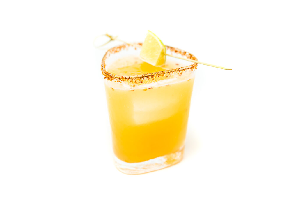 A spicy cantaloupe margarita served in a short glass with a brown sugar and Tajín rim, garnished with a lime wedge on a skewer.