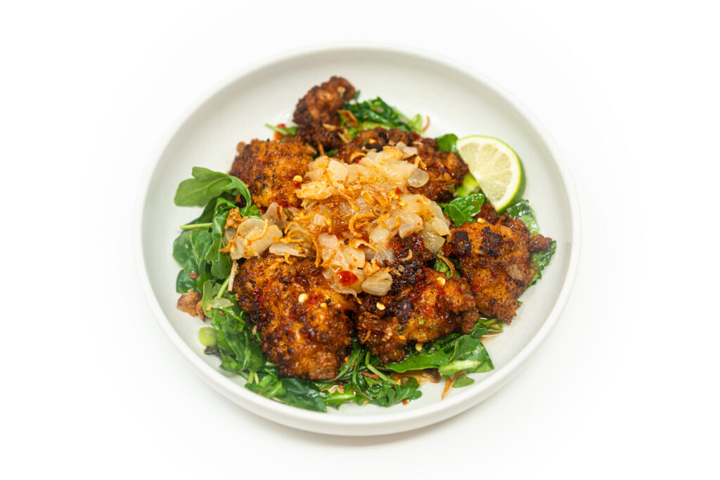 Crispy shrimp fritters drizzled with caramelized sweet onion sauce, served over fresh greens and garnished with lime wedges.