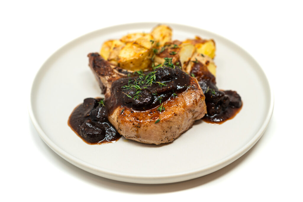 Reverse-seared bone-in pork chop topped with balsamic fig reduction, served on a white plate with fresh thyme garnish
