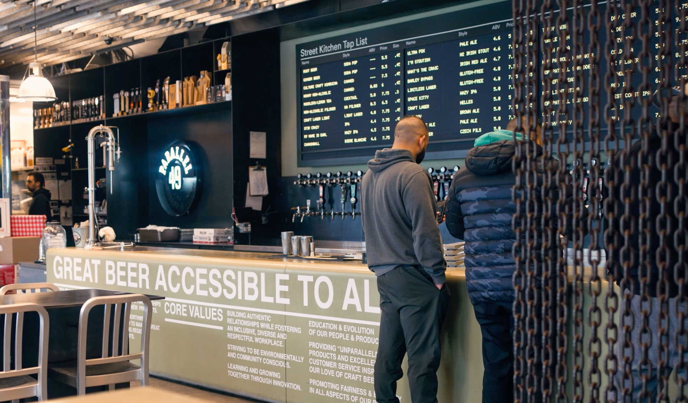 Guests reading the extensive beer list on a blackboard wall at Parallel 49 Brewing’s taproom in Vancouver.