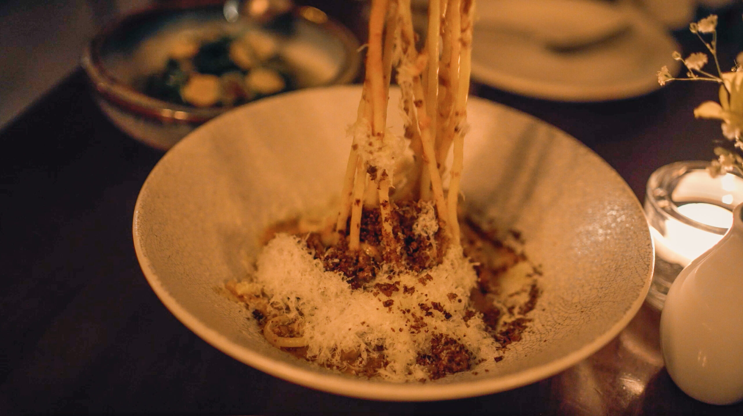 Chopsticks lifting creamy noodles from a ceramic bowl at Kissa Tanto in Vancouver, under moody, intimate lighting.