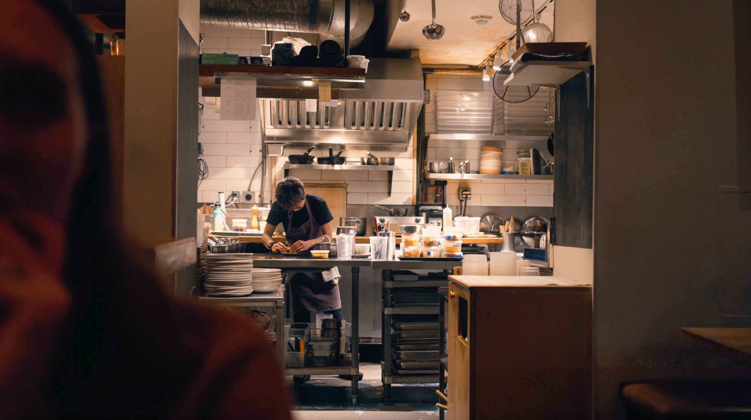 Chef working in the open kitchen at Farmer’s Apprentice in Vancouver, surrounded by warm light and stainless steel.